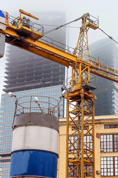 Guindaste no fundo de arranha-céus sob construção em um nevoeiro em um canteiro de obras abandonado — Fotografia de Stock