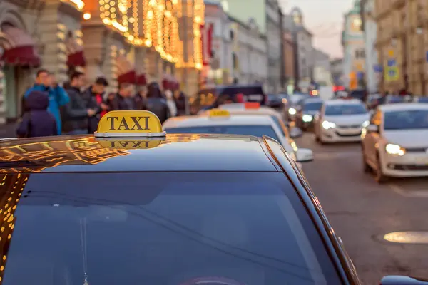 Taksówka zaparkowana na chodniku dużej ulicy z dużymi korkami, samochód odzwierciedla światła nocnego miasta — Zdjęcie stockowe