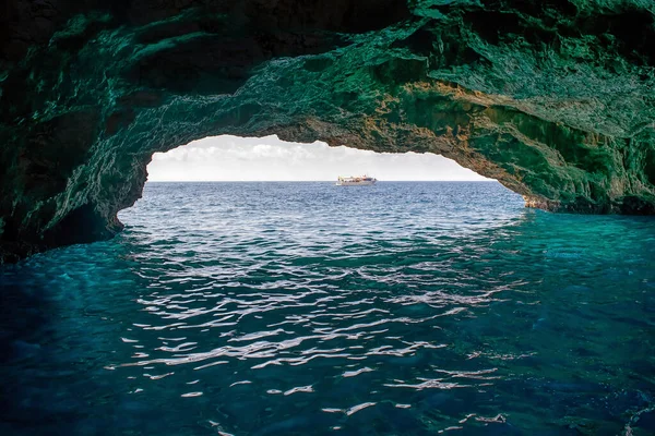 Bir taş mağarada mavi deniz suyu ve ufukta küçük bir tekne ve tünelin sonunda ışık.