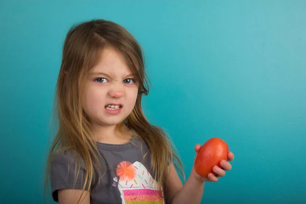 Kleines Mädchen mit unzufriedenem Gesichtsausdruck, das Tomaten hält Stockfoto
