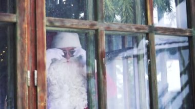 Noel Baba pencereden bakıyor. Noel Baba 'nın gözlüklü haliyle dışarıdan eve bak. Xmas zamanı..