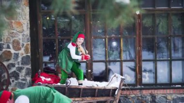 Karda oynayan neşeli elfler. Yeşil takım elbiseli iki neşeli peri büyük pencerenin yanında harika vakit geçiriyorlar. Noel zamanı.