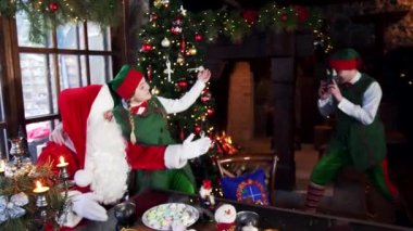 Noel arkaplanında iki elf ve Noel Baba fotoğrafı. Bir elf, Noel Baba 'yla başka bir elfin retro kamerada fotoğrafını çekiyor..