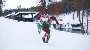 Yeşil peri kostümlü mutlu elfler kışın dışarıda. Orman arka planında nehir kenarında kartopu oynayan iki sevimli elf..