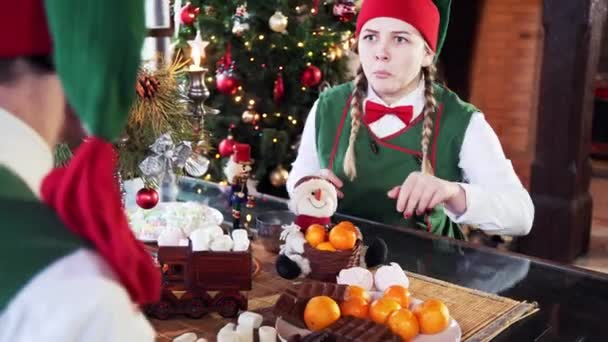 Zwei Lustige Elfen Sitzen Tisch Vor Weihnachtlichem Hintergrund Elfenmädchen Versucht — Stockvideo