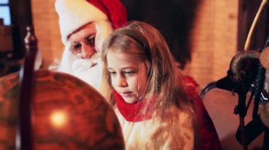 Bir kız Noel Baba 'nın eline oturur ve eski bir küreyi çevirir. Noel Baba 'nın Noel Evi.