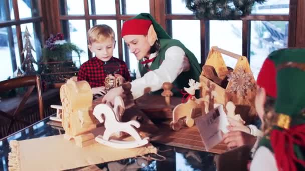 在圣诞老人的住处 一个穿红衫的男孩和一个圣诞精灵玩木制玩具 — 图库视频影像