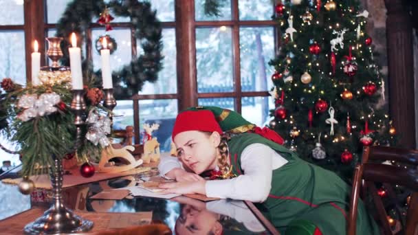 一个穿着绿色西服的小女孩醒来 打呵欠 圣诞老人家 有圣诞树和装饰品 — 图库视频影像