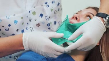 Beyaz lateks eldivenli bir dişçi metal çerçeveli yeşil kauçuk bir baraj yapar. Bir diş kliniğinde tedavi prosedürünün başlatılması.