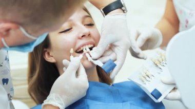 Tıbbi eldivenli bir dişçi ve genç bir kız için takma diş deneyen bir asistan. Diş protezi vitaskalisi için diş tonları paleti..