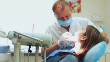Ofiste çalışan bir dişçi. Erkek doktor, sandalyede oturan bir kıza dişlerini tedavi eder..