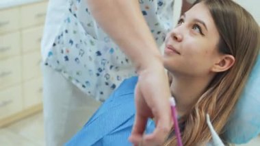 Dişçi sandalyede oturan bir kıza diş önlüğü takıyor. Diş Kliniği.