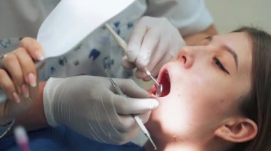 Dişçi muayenehanesindeki kız aynaya bakarken hasta dişler gösteriyor..