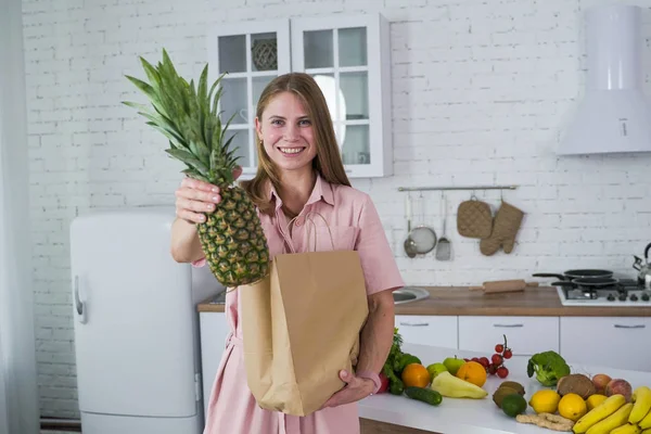En kvinne på et hvitt kjøkken drar ananas ut av en papirpose. . royaltyfrie gratis stockbilder