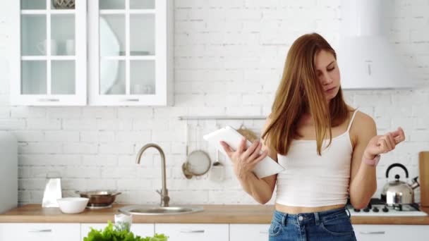 在白色厨房里的女孩手里拿着一块石碑 正在考虑自己的饮食 — 图库视频影像