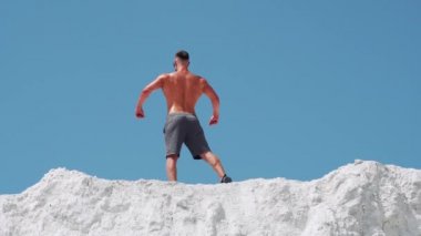 Bodybuilder athlete posing with muscles in nature against a blue sky. A man stands with his back.