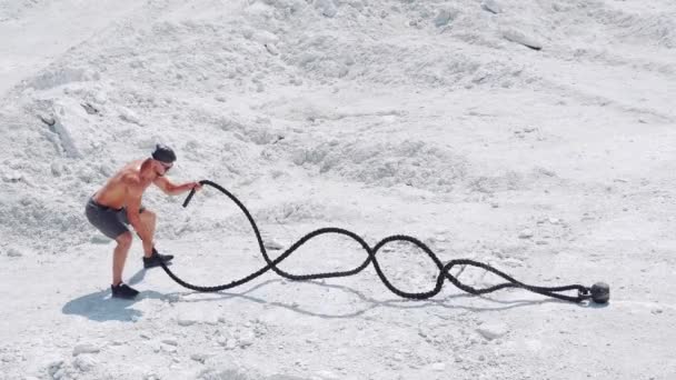Athletic strong man doing exercises with ropes outdoors on the sand. Shirtless bodybuilder training.