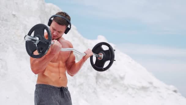 A man in headphones does barbell biceps exercises. Workout in nature. — Stock Footage Man Headphones Does Barbell Biceps Exercises Workout Nature Royalty Free Stock Video
