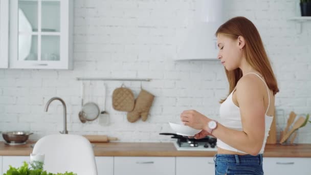 Glückliches Mädchen isst von einem Teller auf weißem Küchenhintergrund. Gesunde Ernährung.