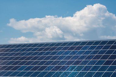 Mavi gökyüzünün arka planında yeşil enerji üretimi için bulutlar bulunan güneş panelleri