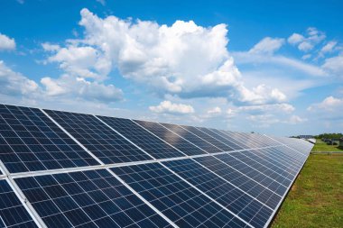Bulutlu ve mavi gökyüzü olan bir alanda bir dizi güneş paneli. Yeşil enerji üretimi