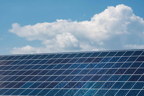 Mavi gökyüzünün arka planında yeşil enerji üretimi için bulutlar bulunan güneş panelleri