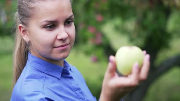 一个穿着蓝色衬衫的小女孩看着手里拿着的苹果 — 图库视频影像