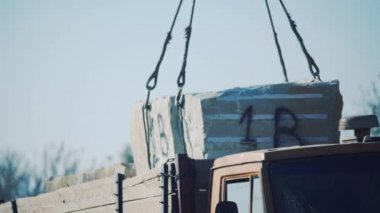 Bir vinç bir kamyon römorkundan bir taş bloğu kaldırır. Fabrikaya kum taşı boşaltılıyor..