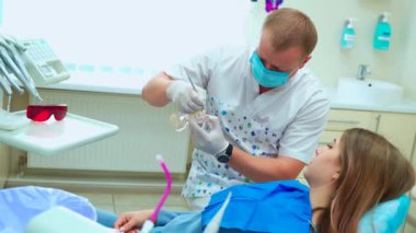 Dişçide genç bir kız çenenin düzenini inceliyor. Maskeli ve lastik eldivenli bir doktor tedavi prosedürünü açıklıyor..
