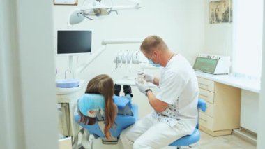 Dişçi randevusundaki sandalyedeki kız. Ofisteki doktor, hastaya diş çene düzenini gösterir..