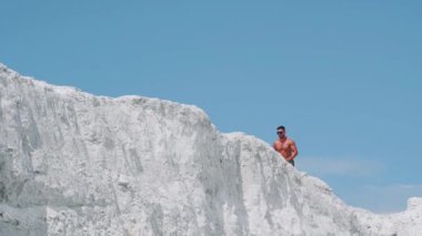 Üstsüz, kaslı bir erkek vücut geliştirici mavi gökyüzüne karşı beyaz bir dağ boyunca koşar..
