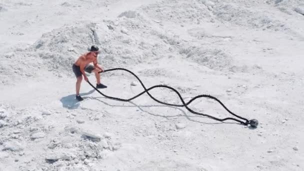 Muž kulturista dělá intenzivní atletické cvičení s provazy. Školení o přírodě na bílém písku.