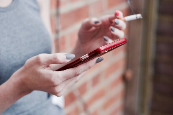 Женщина курит и проверяет телефон
