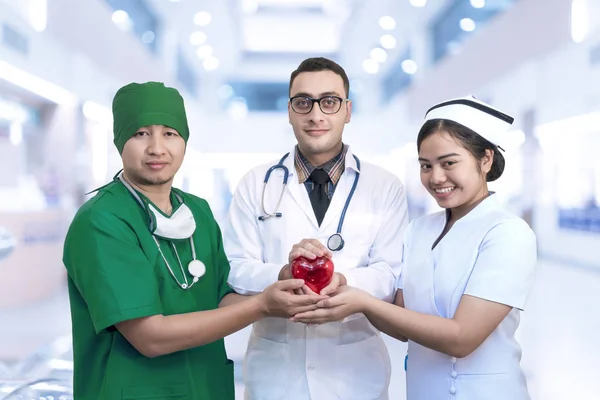 Equipe de médicos jovens e enfermeira segurando forma de coração vermelho — Fotografia de Stock