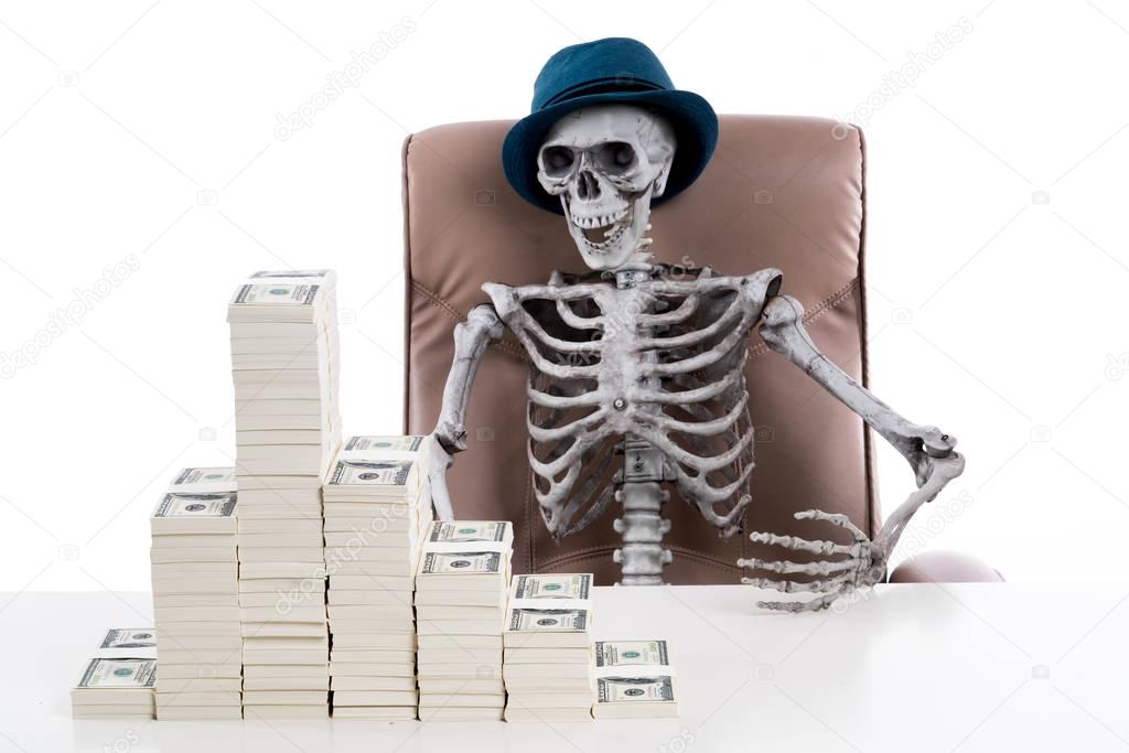 Human skeleton sitting in a big chair with stack of banknote on 