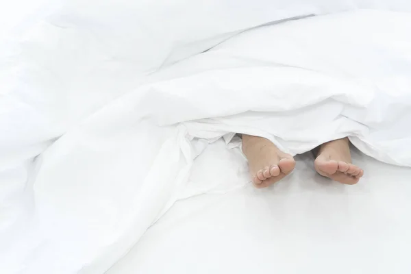 Fötter under vita täcket på säng — Stockfoto