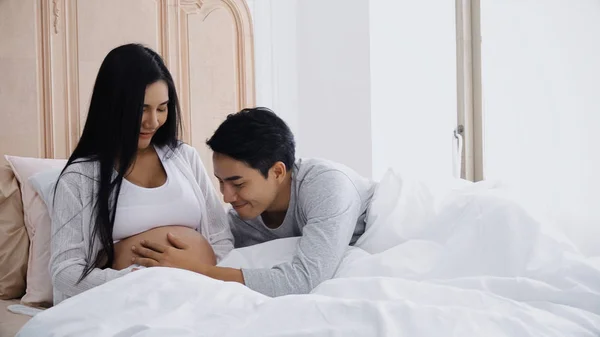 Jovem marido tocando barriga de sorrir esposa grávida na cama — Fotografia de Stock