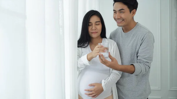 Молодой человек и беременная жена у окон с занавесками — стоковое фото