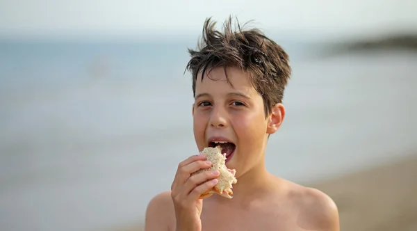 Trevlig kille medan man äter en smörgås på stranden — Stockfoto