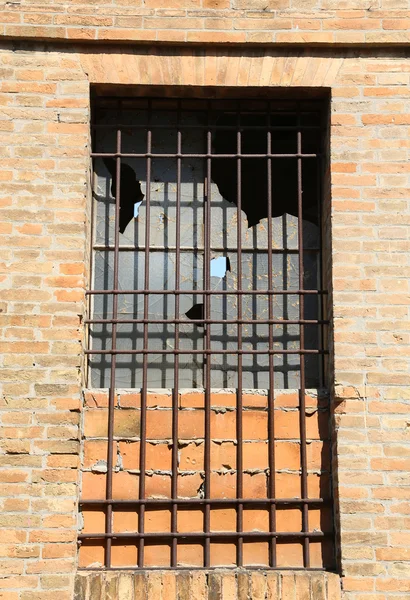Разбитое окно заброшенного дома с железными решетками — стоковое фото