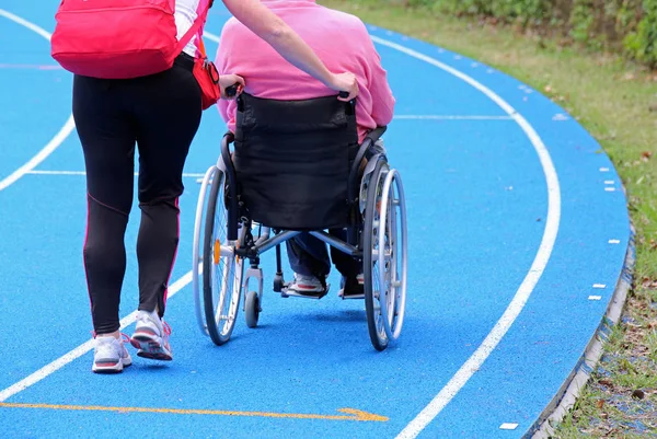 Bir tekerlekli sandalye üzerinde özürlü kişi üzerinde atletik bir Yardımcısı ile — Stok fotoğraf