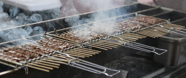 grilled meat with a lot of smoke in a street food stall