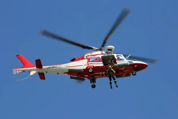 Bomberos volando en helicóptero mientras un bombero desciende con el winc — Foto de Stock