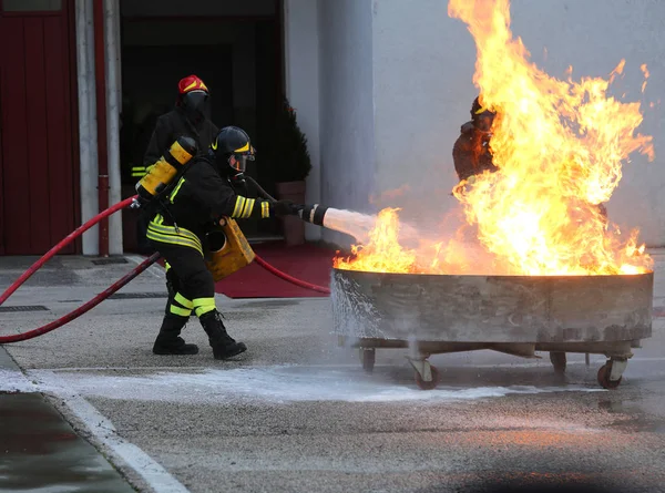 Bomberos con tanque de oxígeno extinguiendo un fuego con espuma — Foto de Stock