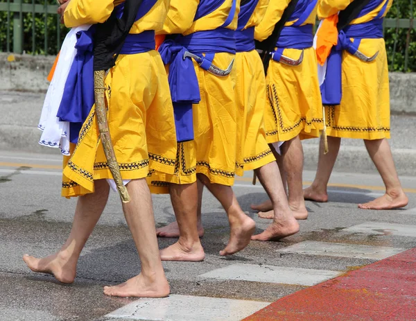 Five men of Sikh Religion with long dresses walking barefoot