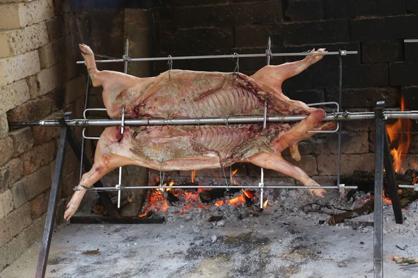 Pig cooks slowly on enormous steel spit in the gigantic fireplac — Stock Photo, Image