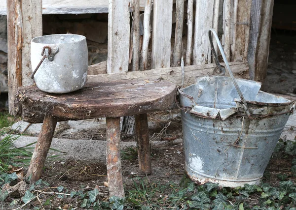 Old broken bucket and an aluminum pan on the wooden stool that w — Stock Photo, Image