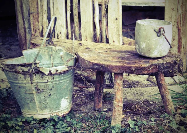 Broken bucket and an aluminum pan on the wooden stool — Stock Photo, Image
