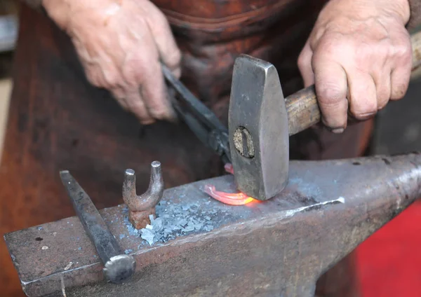 Mãos de um ferreiro idoso trabalhando ferro com um martelo e th — Fotografia de Stock