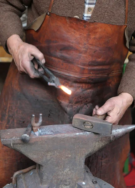 Руки пожилого кузнеца, работающего утюг с молотком и й — стоковое фото